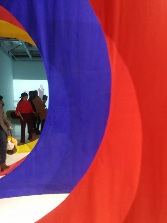 des drapés de couleur rouge et bleu, une vidéo et des visiteurs de l'exposition