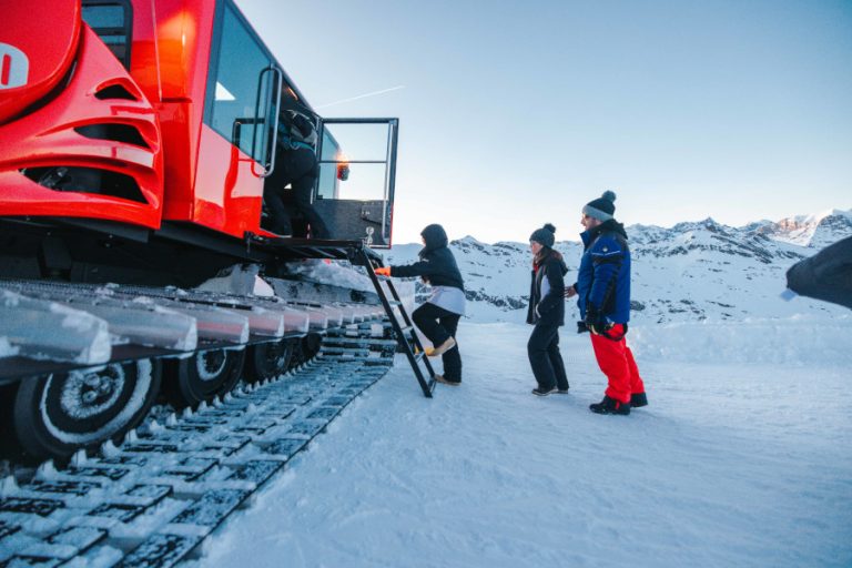 Des touristes montent dans la dameuse sur fond de neige