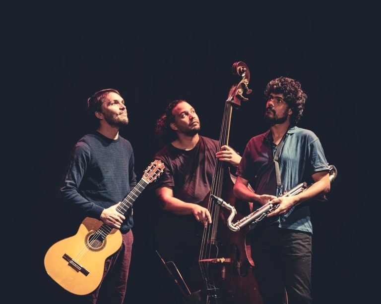 3 musiciens sur fond noir regarde au-dessus d'eux