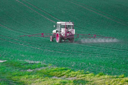 Tracteur pulvérisant des pesticides sur un champ de blé. 