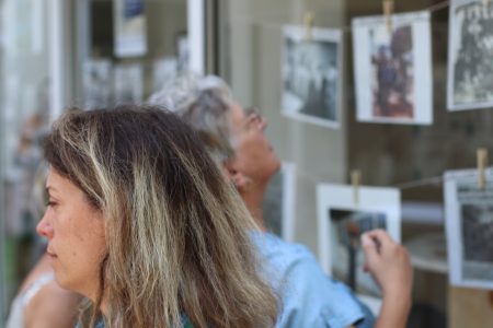 Une femme de profil à l'avant de la photo, et en arrière plan une autre personne regardant des photos exposées sur une vitrine