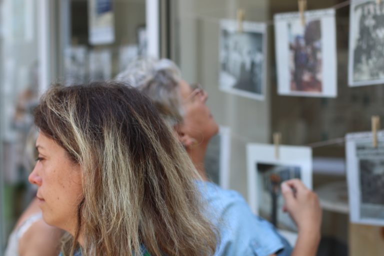 Une femme de profil à l'avant de la photo, et en arrière plan une autre personne regardant des photos exposées sur une vitrine