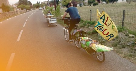 dans la campagne, des vélos avec remorque et dreapeau fait main sur lequel on lit altertour 
