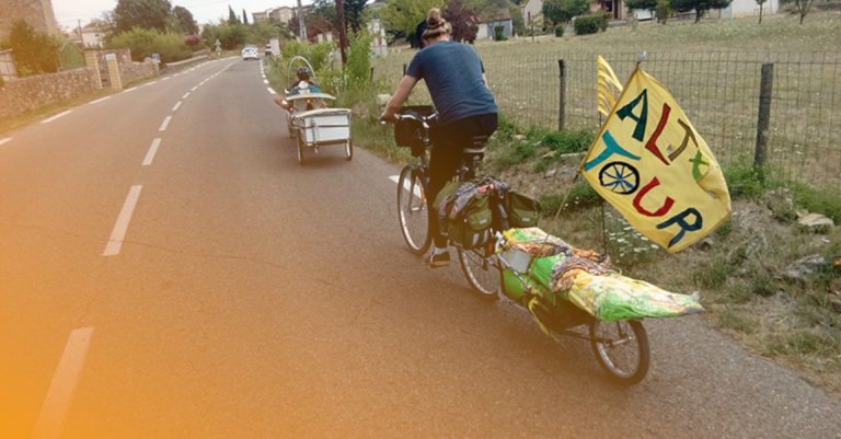 dans la campagne, des vélos avec remorque et dreapeau fait main sur lequel on lit altertour 