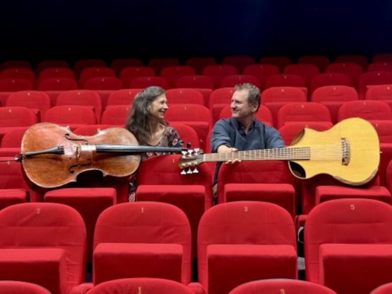 deux musiciens avec guitare bass et violoncelle dans des fauteuils rouges au milieu d'une salle de cinéma