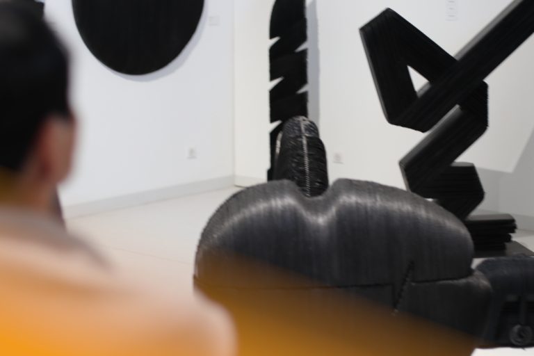 Des sculptures noires dans une pièce blanche et une personne regardant.