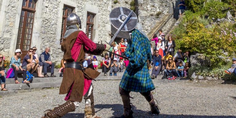 deux combattants habillés en tenue du moyen-âge se battent avec épées et bouclier dans la cour du château