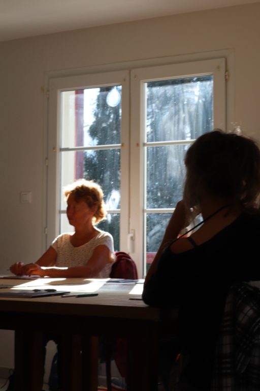 Le soleil traverse la fenêtre pour se poser sur les cheveux d'une femme et une table où sont posés feuilles blanches et crayons