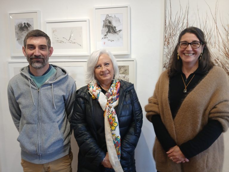 1 homme et 2 femmes souriant devant des tableaux et photographies 