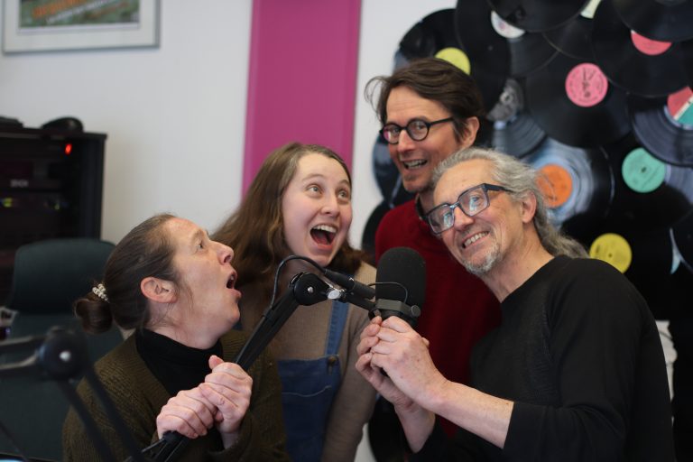 2 femmes et un homme chantent et sourient devant un micro dans un studio radio