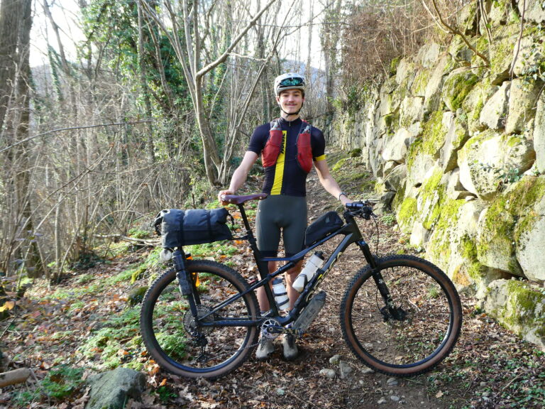 Un jeune homme posant derrière son VTT en pleine nature